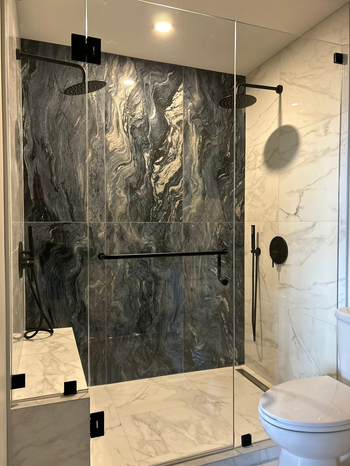 Frameless glass shower with dark stone tile and a built-in bench